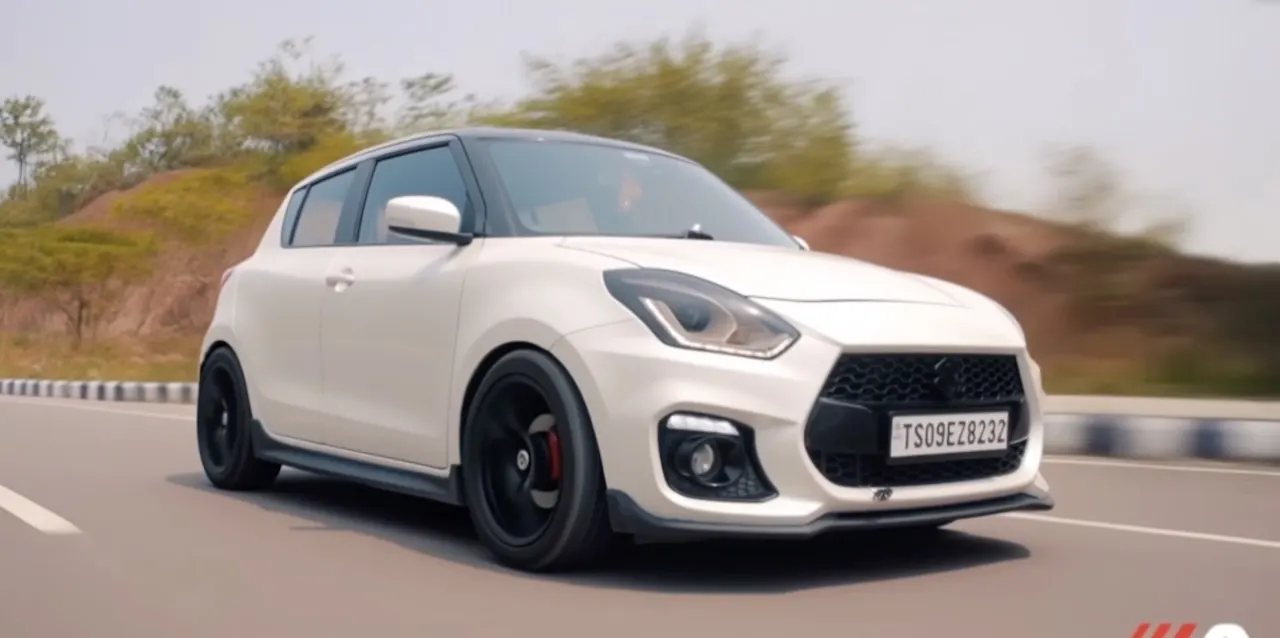A white Suzuki Swift driving on an open road.